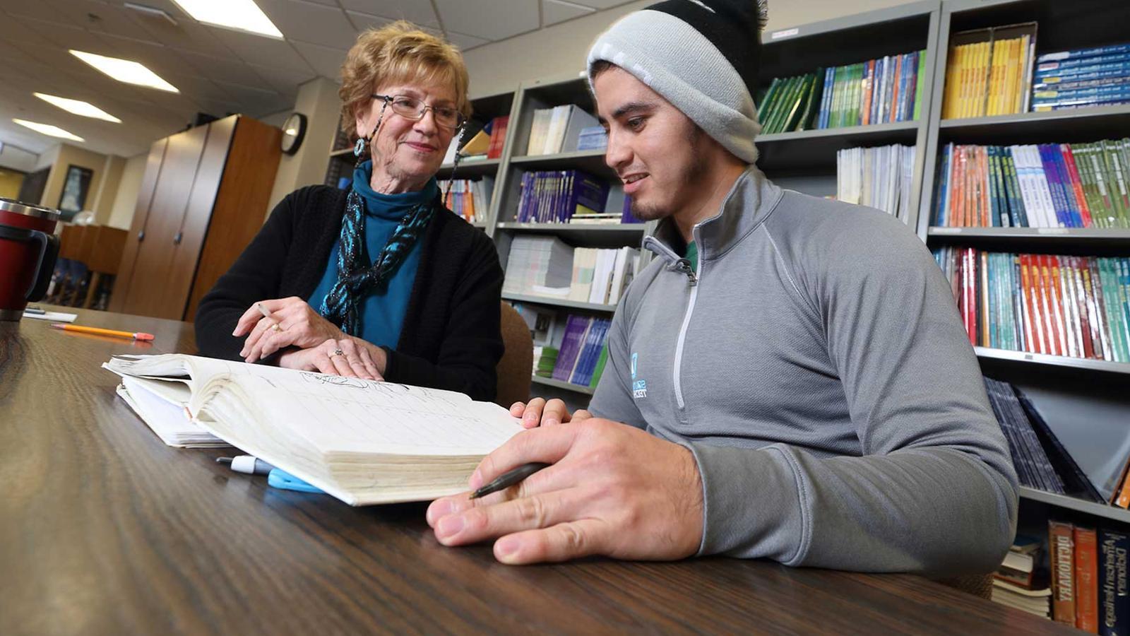 Student with teacher and open book at large table